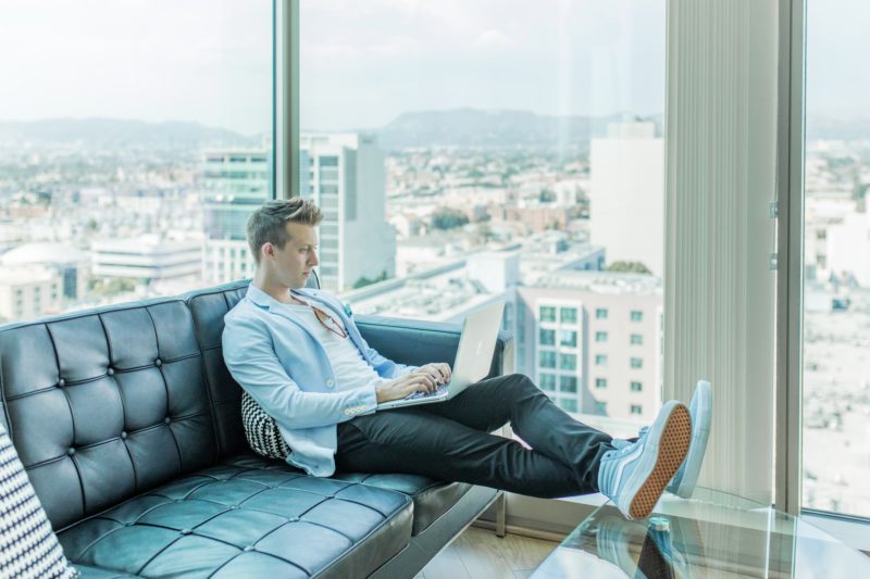 homem no sofá com notebook no colo trabalhando de forma remota com benefícios corporativos